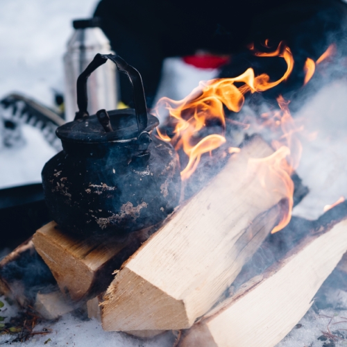 Closeup shot of a metal teapot on burning wood in the winter in the north of Sweden